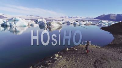 Aerial View Of A Woman Standing Along The Shore Of A Glacier Lagoon, In The Arctic At Jokulsarlon Glacier Lagoon, Iceland - Video Drone Footage