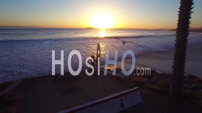 Aerial View Over A Woman Standing With A Surf Board Looking Out At The Sunset - Video Drone Footage
