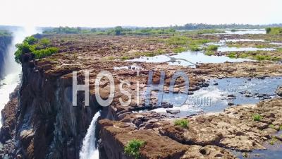 Aerial View Of A Man And Woman Sitting In Devil's Pool Waterfall At Victoria Falls Zambia - Video Drone Footage