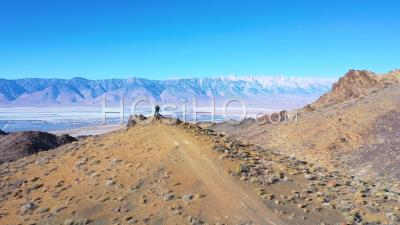 Man Stands On The Edge Of A Vast Open View Of The Owens Valley Desert And Owens Lake Bed In The Eastern Sierras Of California - Aerial Video By Drone