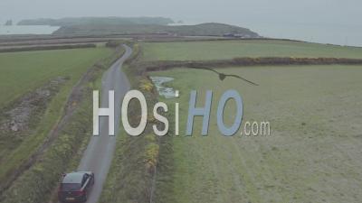 Black Car Speeding On A Country Road Surrounded By Green Fields, On A Moody Day - Aerial Drone View