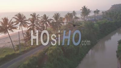 Une Moto Traversant Une Petite Route En Béton à Côté De La Plage De Varkala Sous Le Coucher Du Soleil Au Kerala, Inde - Vue Aérienne Par Drone