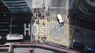People Crossing On The Yellow Pedestrian Lane At The Intersection In Hong Kong While The Vehicles Are On The Lane Have Stopped - Aerial Shot