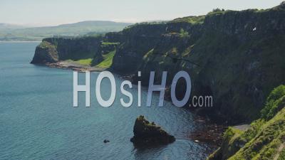 Lush Cliff Surrounded By Dark Blue Sea In Rathlin Island, Ireland With A Bird Flying On A Sunny Day - High Angle Shot
