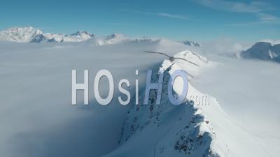 Snow Covered Mountain Ridge Rising Above The Clouds - Video Drone Footage