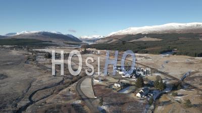 Dalwhinnie Distillery And Dalwhinnie Town With Ben Alder And Loch Ericht In The Background - Video Drone Footage